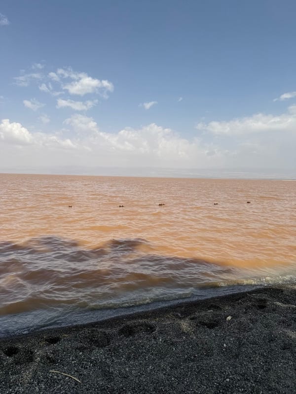 A wide lake under clouds, a dark sand shore