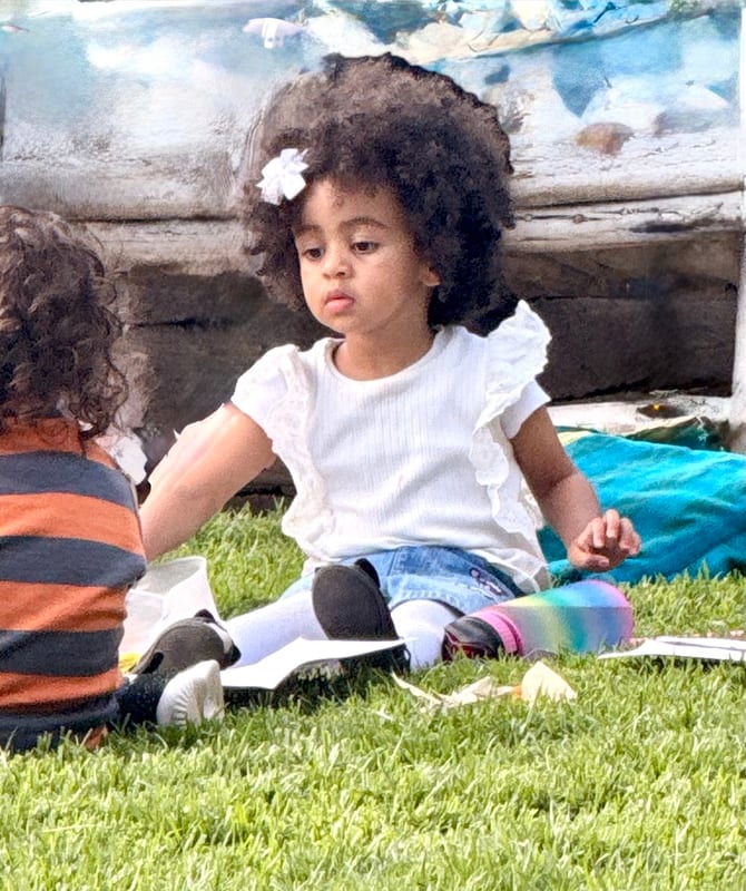 A little girl with a flower in her hair, sitting on the grass