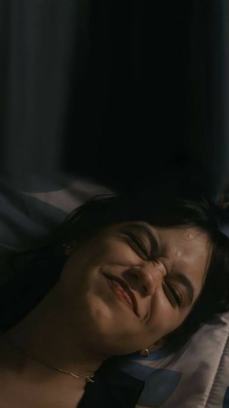 Someone laughing in bed, eyes squeezed shut