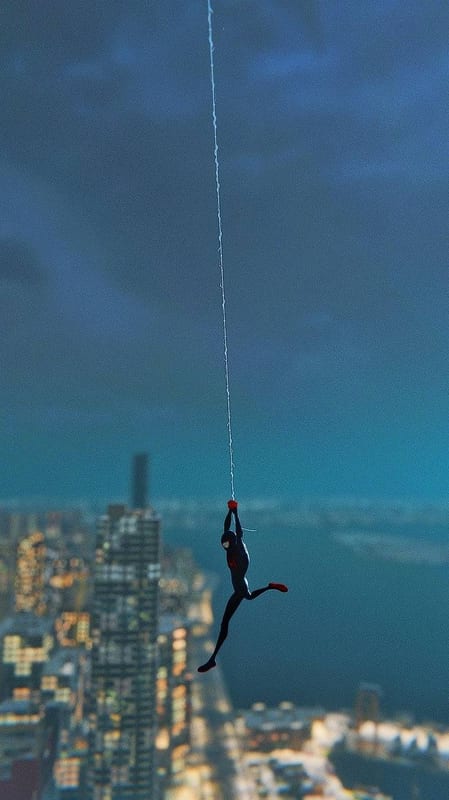 Spider-Man hanging from a line over the city at dusk