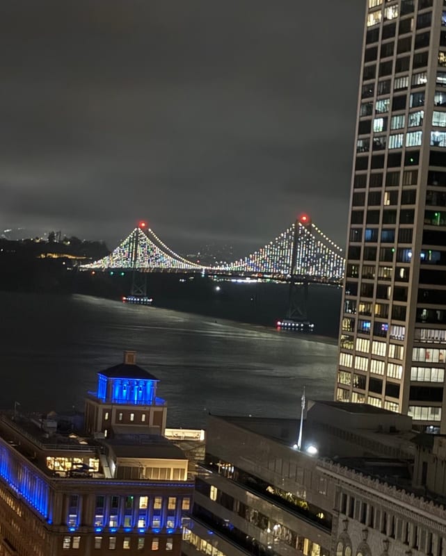 The Bay Bridge lit up at night, a blue-lit building below