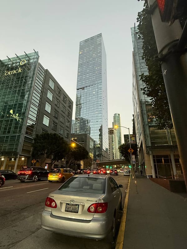 Glass towers over a street, a parked sedan