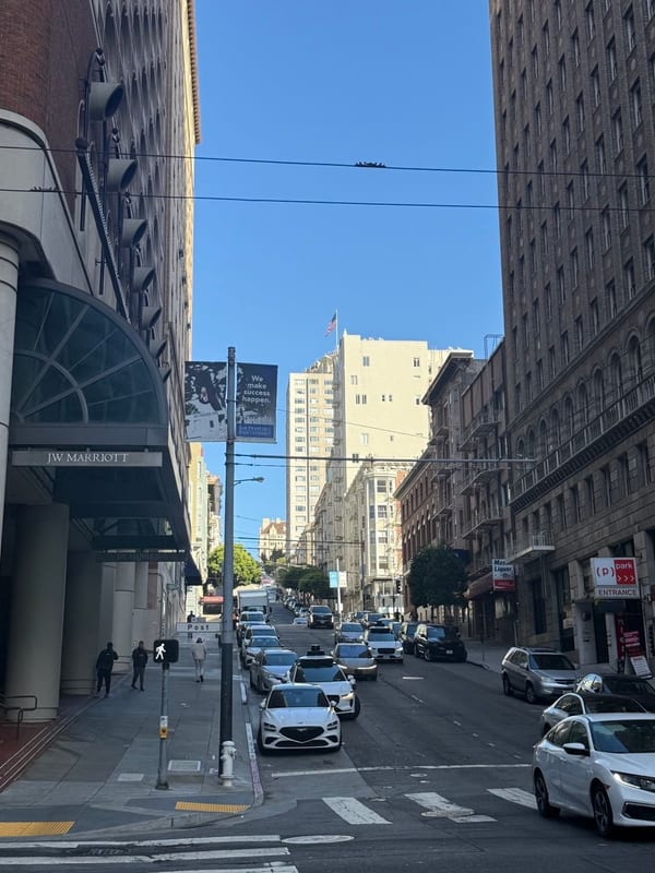 A street climbing a hill past the JW Marriott, cable car wires overhead