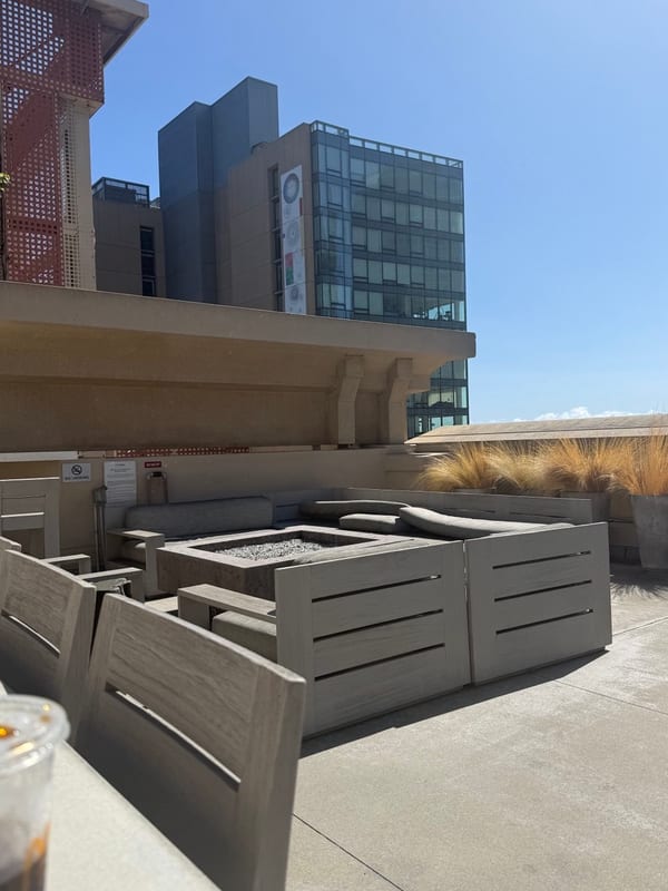 A rooftop with stone seats around a fire pit, towers behind