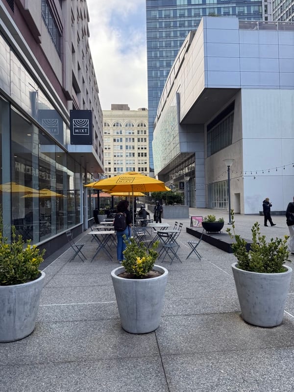A lane of yellow umbrellas and potted trees between towers